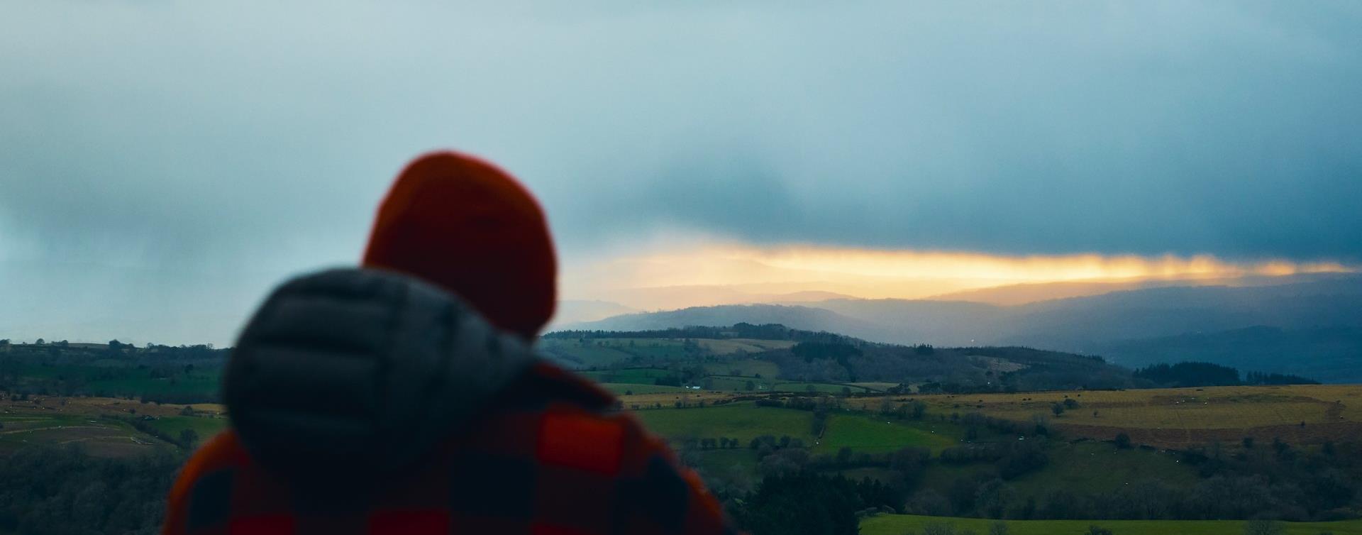 A walker in a red check jacket looking over the valley from Hay Bluff at dusk