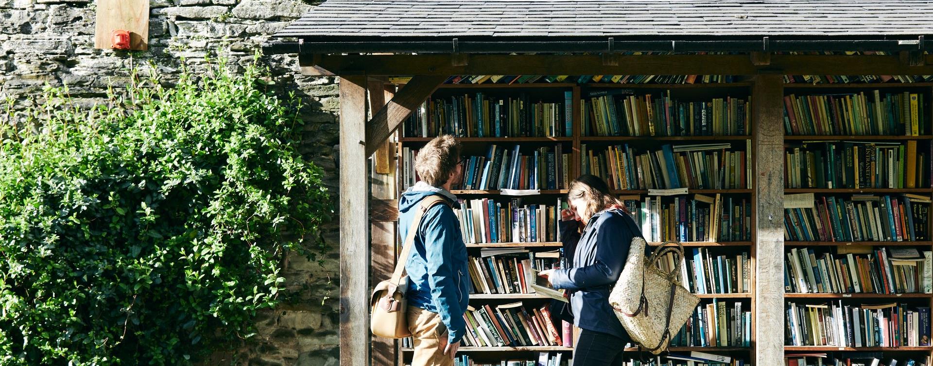 Two people browsing the outdoor honesty bookshelves in Hay-on-Wye