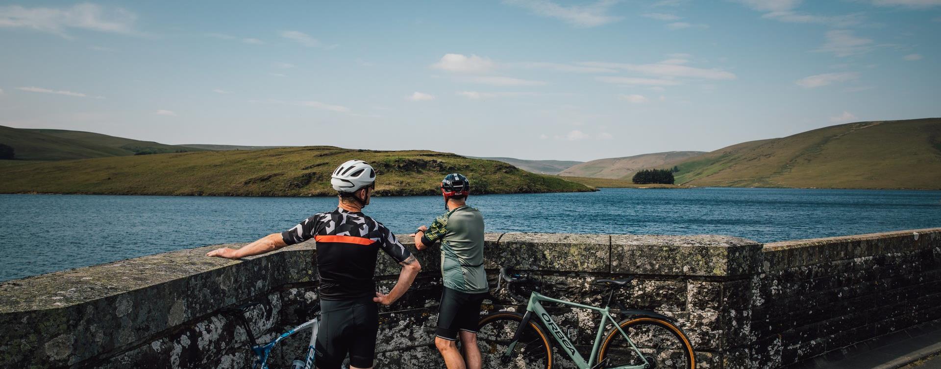 Two cyclists resting their bikes against the wall of a dam above an Elan Valley reservoir