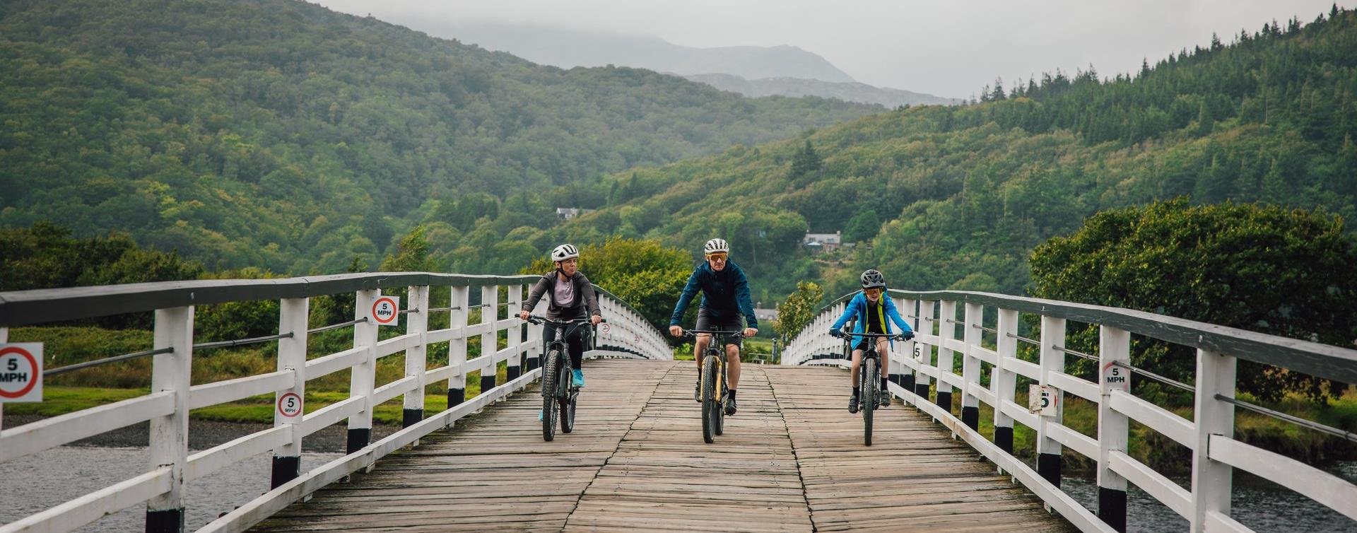 Three cyclists riding towards the camera over the wooden toll bridge at Penmaenpool on the Mawddach Trail