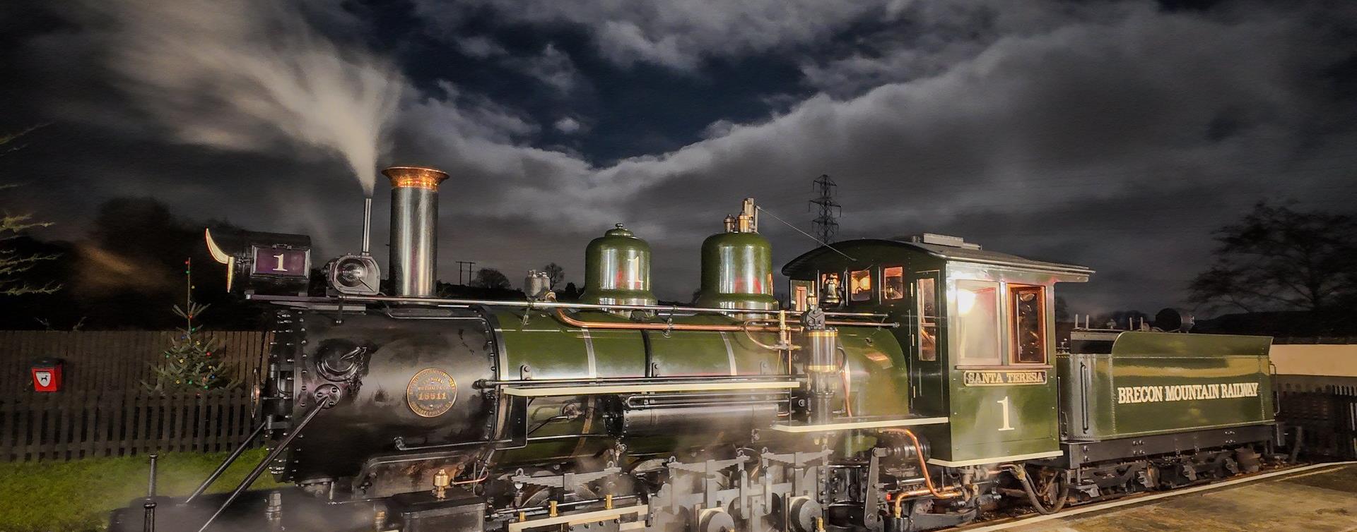 A green steam engine letting off steam on the platform at night under a moonlit sky