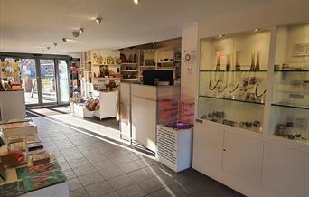 gallery shop inside view toward an entrance door. There are glass shelves on the right with jewelry inside and white plinths with books and cards of t