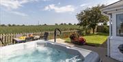 The beautiful, bubbling hot tub is in the foreground with the lawn stretching away. The patio dining table and chairs overlook the countryside