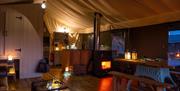 The lounge and dining area of the inside of Afon safari tent, with trunk coffee table, the fire light and dining table in the foreground