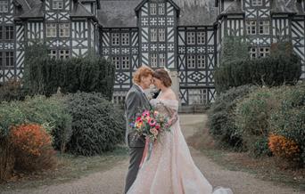 Two women in wedding outfits in front of a black and white stately home