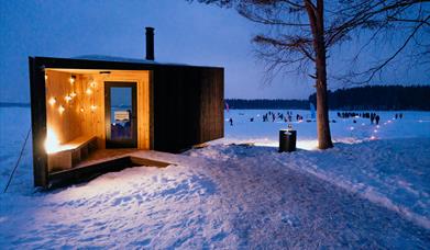 Dagsturhytte som lyser opp med barn som leker på isen bak