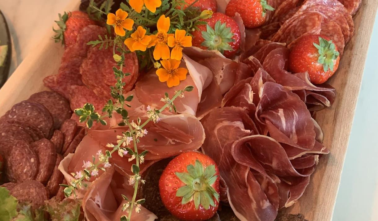 Et stort serveringsfat fylt med ulike typer spekemat, grønnsaker og pyntede urter.