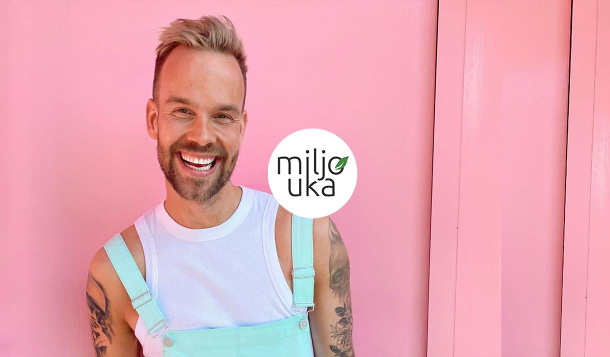 Morten Hegseth med grønn selebukse smiler bredt til kamera. Sjokkrosa bakgrunn.