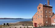 Brick building at the water’s edge on a clear day with blue sky.