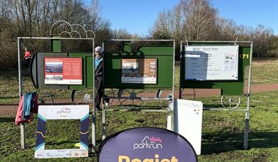 Rogiet Parkrun sign in Rogiet countryside park with runners in background sunny day in monmouthshire
