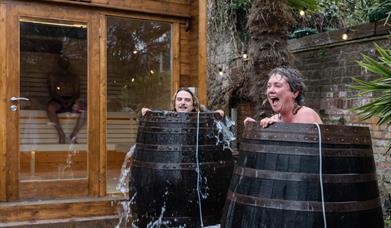 Woman and man laugh in cold plunge as cold water spills out of cold plunge barrel in Stone Rock Lodge 