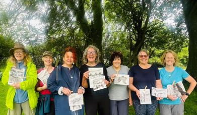 Women holding their artwork under a tree