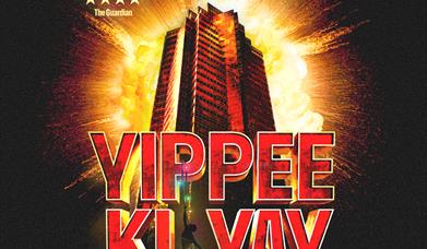A man hanging off the title Yippee Ki Yay. Behind is a building and explosion.