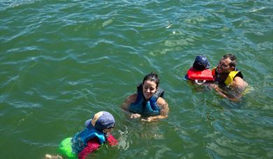 Mother and father with two children playing in the water wearing buoyancies