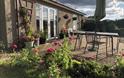 Front view of Blackthorn Lodge showing the lounge patio doors, front door and patio garden area with garden furniture including a table, 4 chairs, par