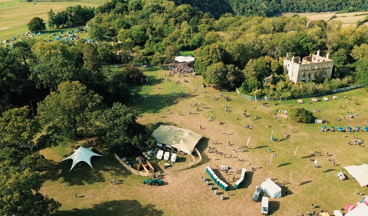 Into The Woods Festival UK  ariel shot looking down of field of green grass and woods and festival tents and people