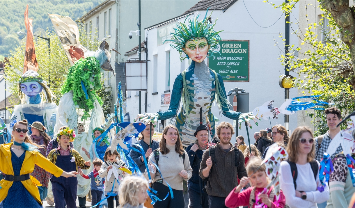 Photograph of people, puppets and flags walking down Monmouth high street during Wye Valley River Festival