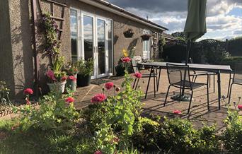 Front view of Blackthorn Lodge showing the lounge patio doors, front door and patio garden area with garden furniture including a table, 4 chairs, par