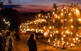 People standing looking at a sculpture lit up with flames
