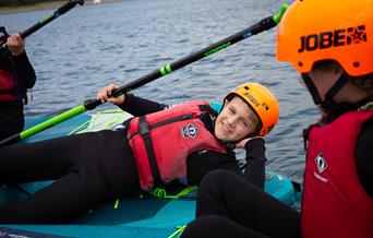 Child lying across a paddle board smiling
