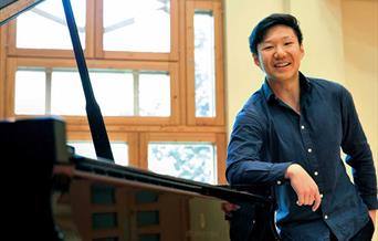 Noah Zhou leaning against piano