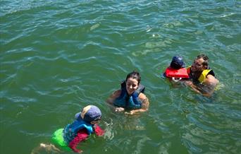 Mother and father with two children playing in the water wearing buoyancies