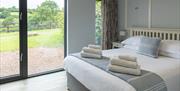 The Sugar Loaf master bedroom with French door and large windows looking out across the valley. The king-size bed has clean white towels folded on it,