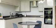 The Skirrid kitchen and living area, with a table and two chairs, a mid-height double oven, an electric ceramic hob, tea and coffee making facilities,