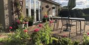 Front view of Blackthorn Lodge showing the lounge patio doors, front door and patio garden area with garden furniture including a table, 4 chairs, par