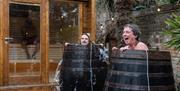 Woman and man laugh in cold plunge as cold water spills out of cold plunge barrel in Stone Rock Lodge