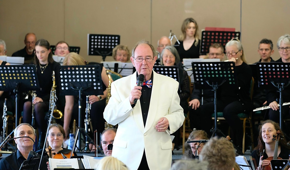 Male conductor in a cream jacket standing in front of an orchestra
