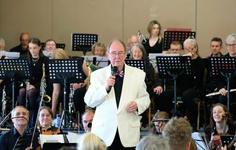 Male conductor in a cream jacket standing in front of an orchestra