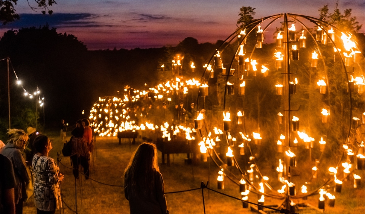 People standing looking at a sculpture lit up with flames