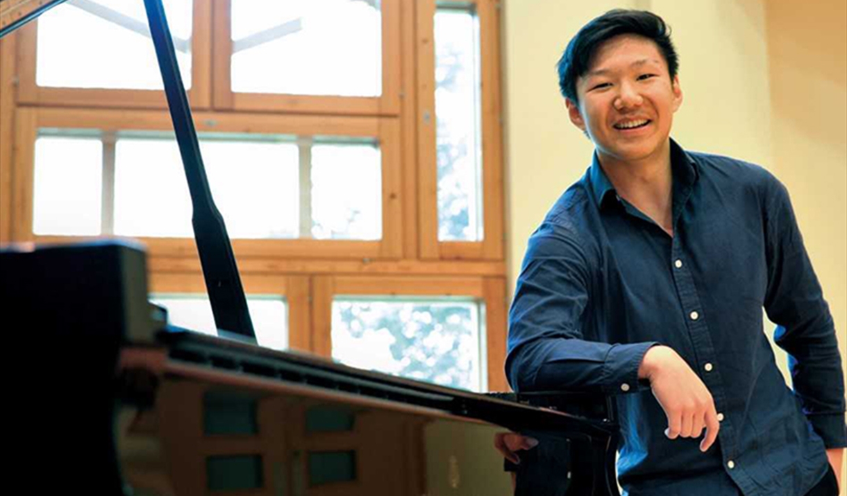 Noah Zhou leaning against piano