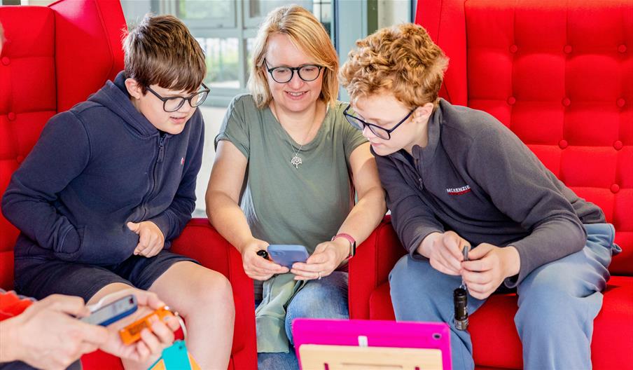 A photograph of two boys and a woman smiling and looking at an tablet screen on a coffee table.