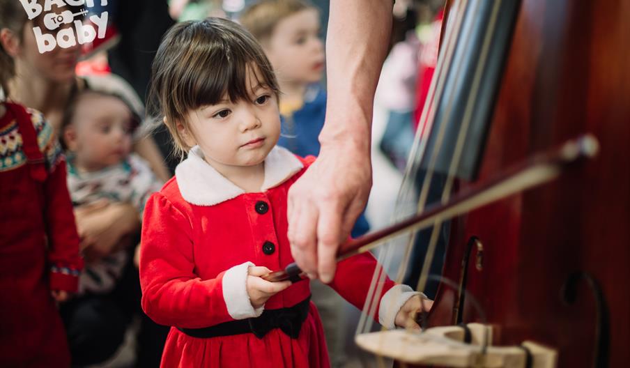 toddler inspects a cello at a bach to baby christmas concert