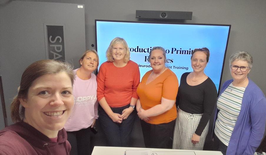 A group of therapists including two osteopaths, a cranial sacral therapist, a massage therapist and a homeopath standing in front of a screen that say