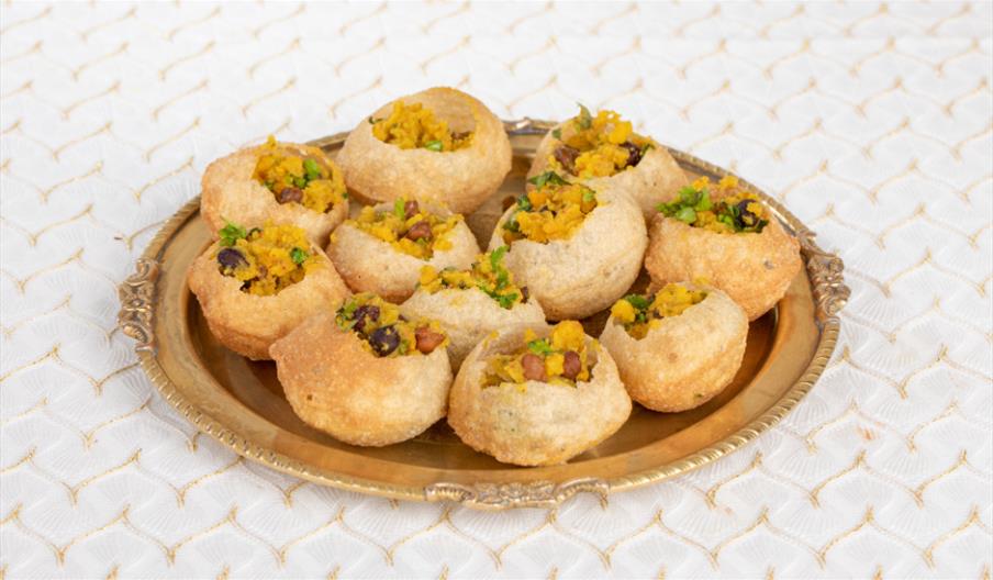 A plate of small puris (fried hollow crisps) filled with potatoes.