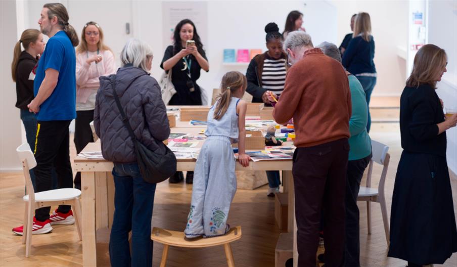 People around long tables in the gallery, making and talking
