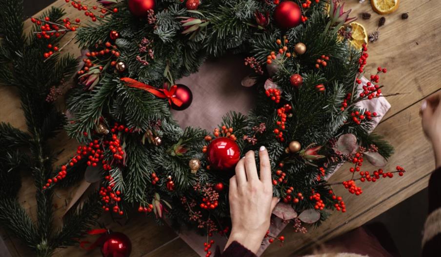 A  hand making a Christmas Wreath on a wooden table.