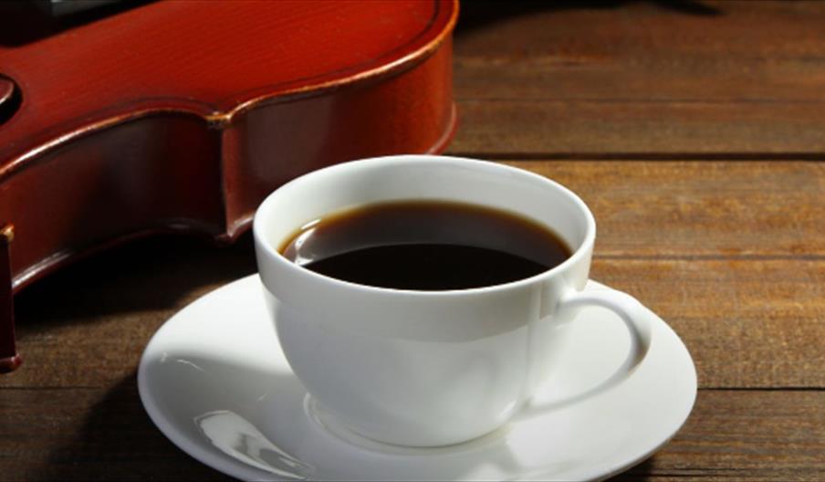 A coffee cup on a wooden table. There is a violin in the background.