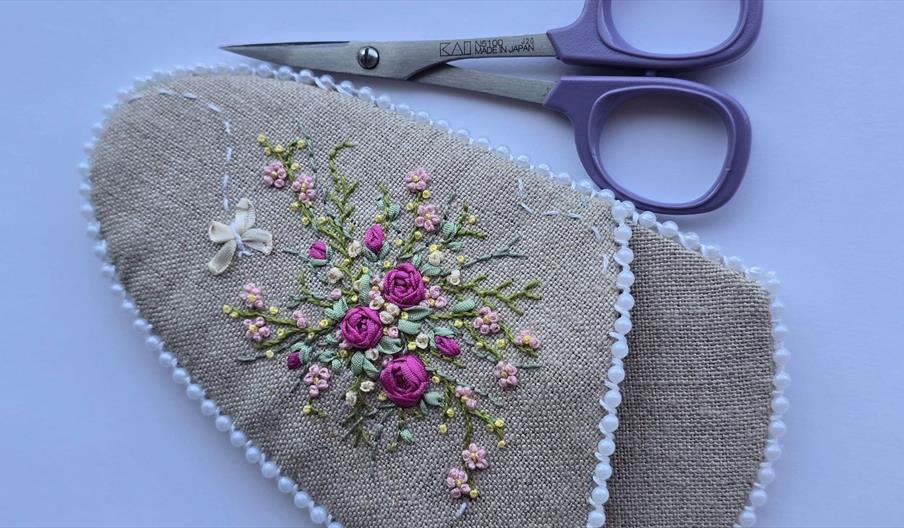 A pair of scissors pictured next to an embroidered pouch, stitched with pastel colored flowers
