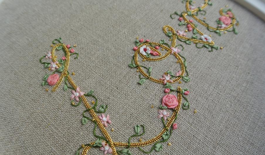 A close-up image of an embroidered cloth that reads 'love', adorned with embroidered flowers