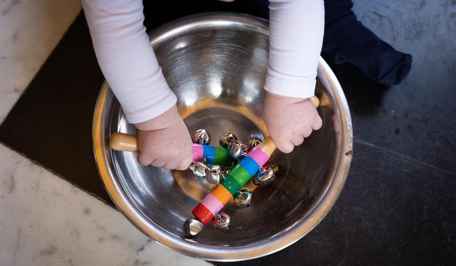 Childs hands holding bells in a metal bowl.