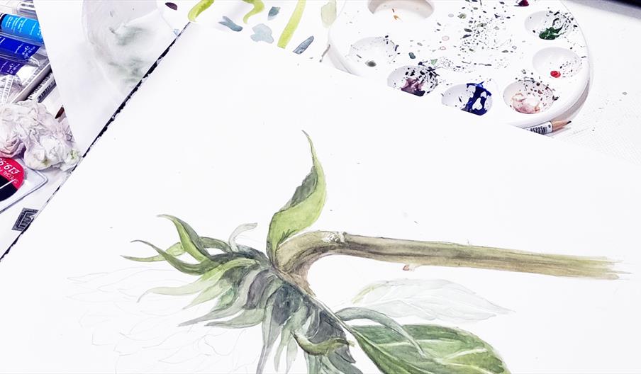Watercolor painting of a sunflower pictured on an open notebook