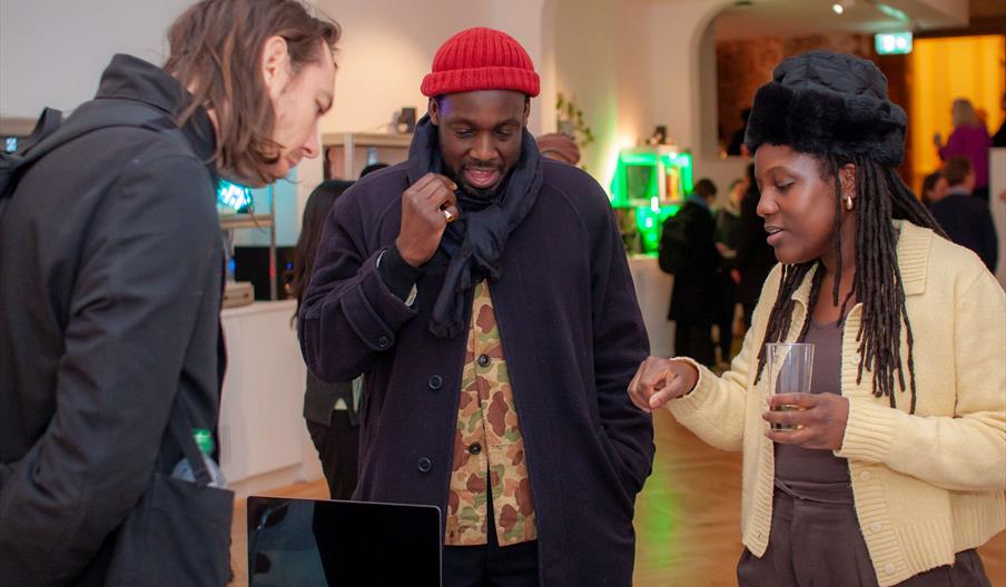 Three young people stood together chatting in a gallery space.