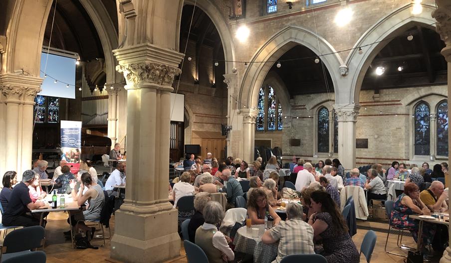 Groups of people sit round tables taking part in a quiz night in a historic church