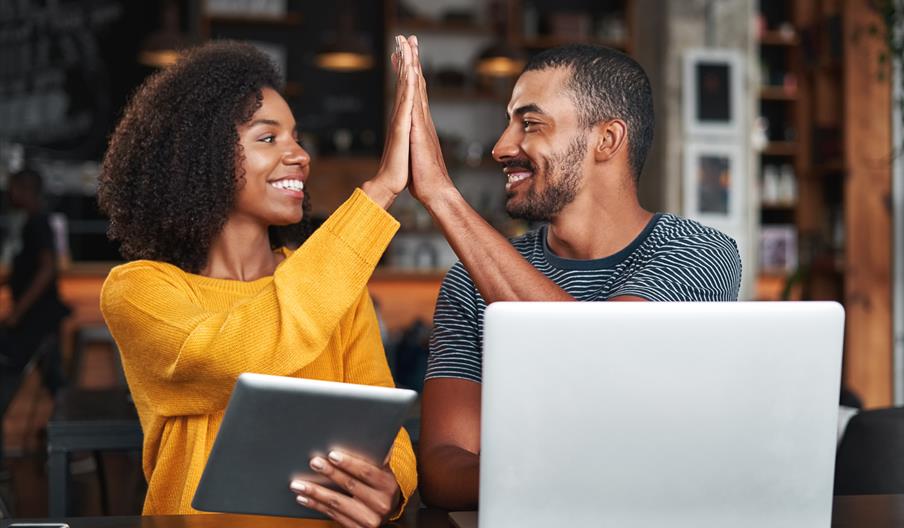 Man and woman high fiving each other in front of a tablet and laptop.
