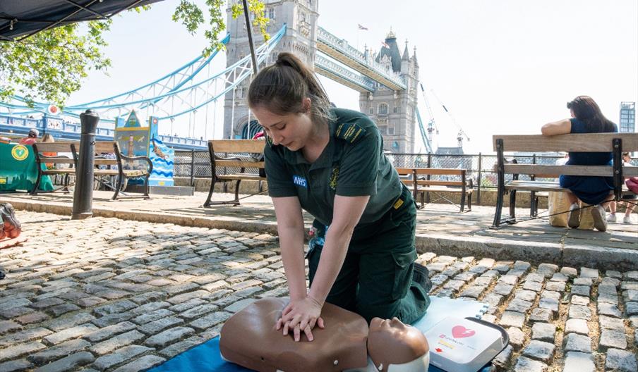 A LAS paramedic demonstrating CPR on a dummy in front of Tower Bridge