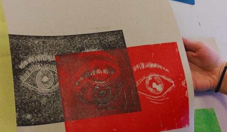 An image of someone  holding up two prints, both of a pair of eyes, one in red and one in black